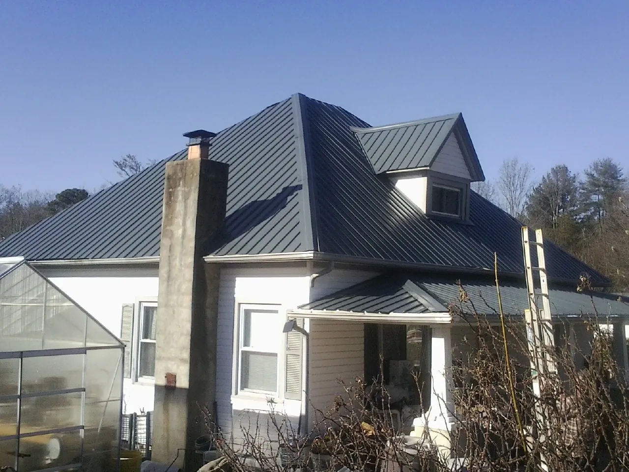 Dark blue standing seam metal roof on a white farmhouse with dormer — Slate & Tile Roof Repair by Roofing Brothers in Peterman