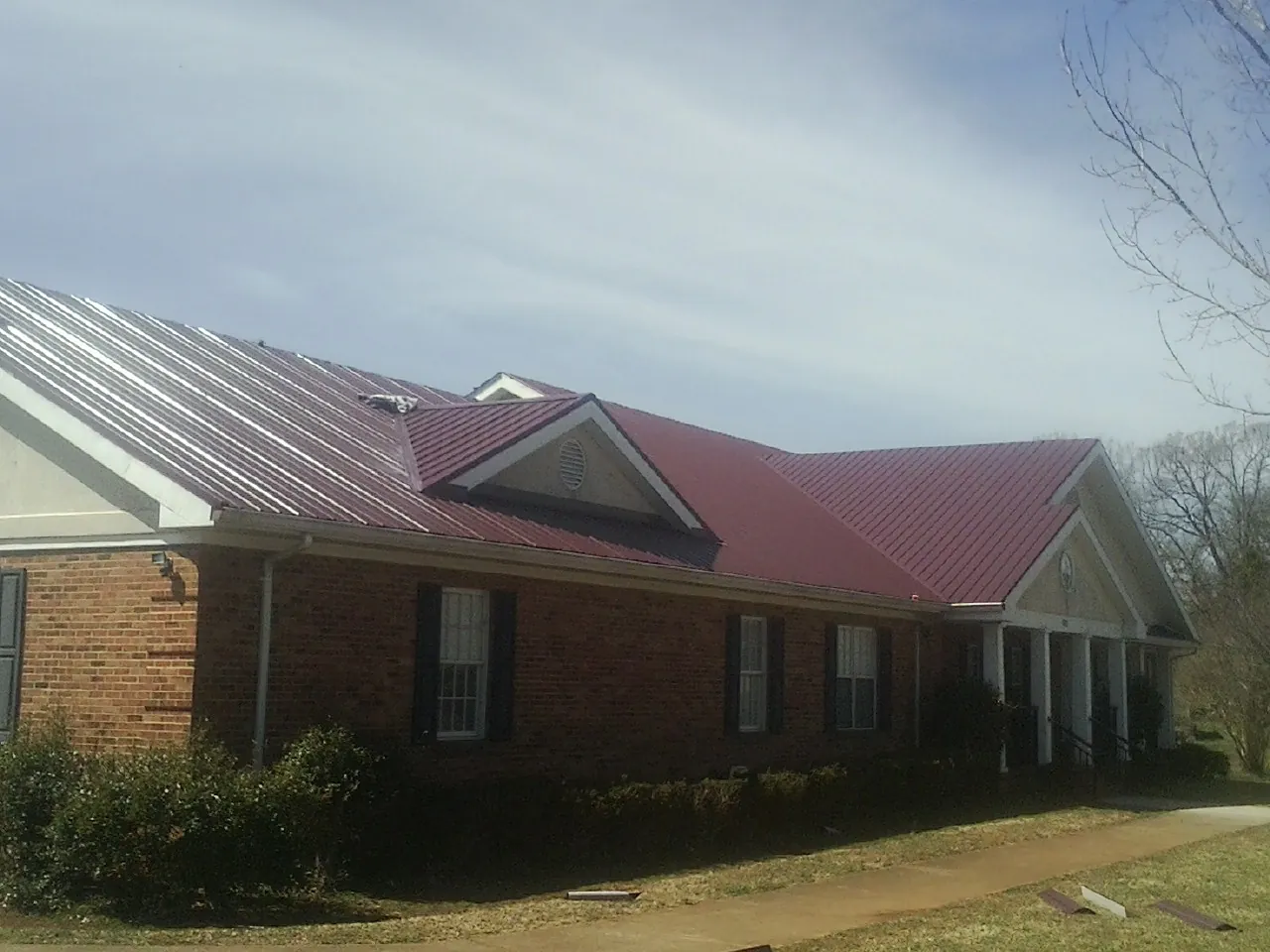 Red metal roof with gabled entries on a long brick building, from a Hail Damage Roof Repair job in Peterman
