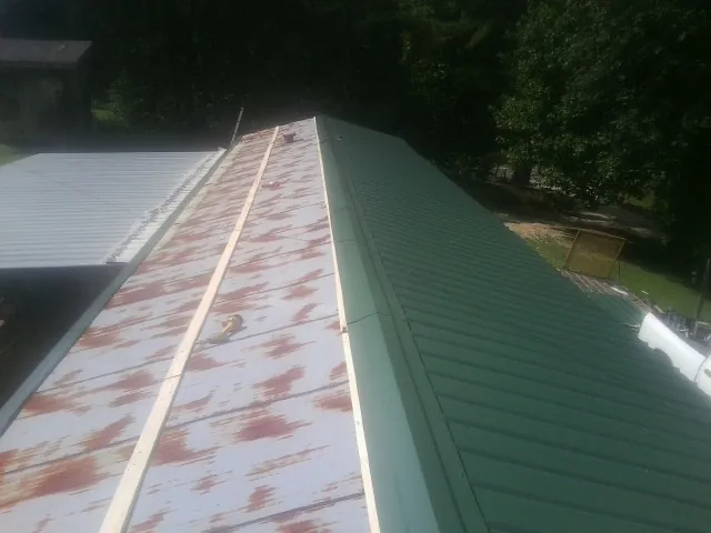 Old rusted panels beside newly installed green metal roofing — Wind Damage Roof Repair by Roofing Brothers in Peterman