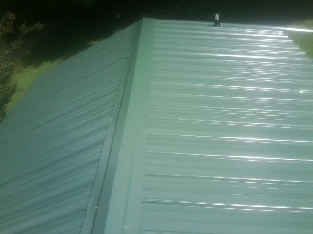 New green metal panels meeting at the ridge of a roof — Flat Roof Repair work by our crew in Peterman