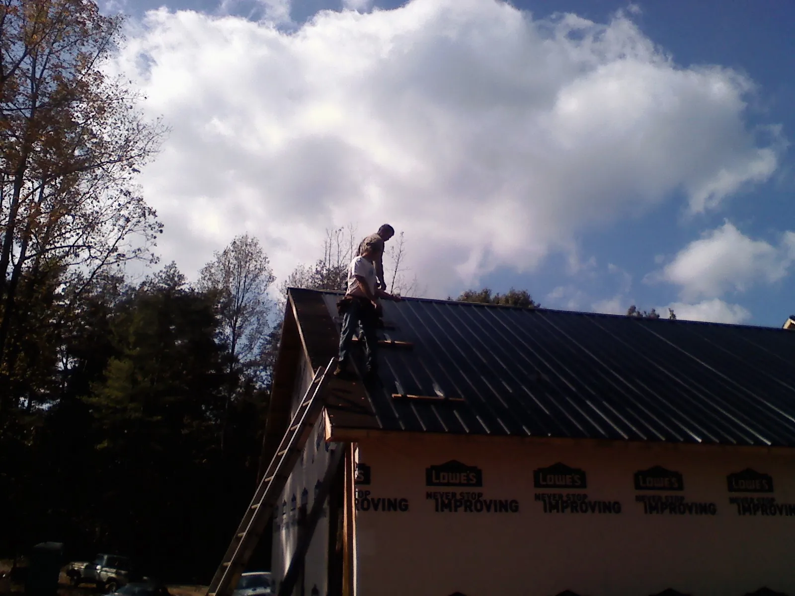 Roofer fastening dark metal panels high against a cloudy sky, from a Roof Inspection job in Peterman