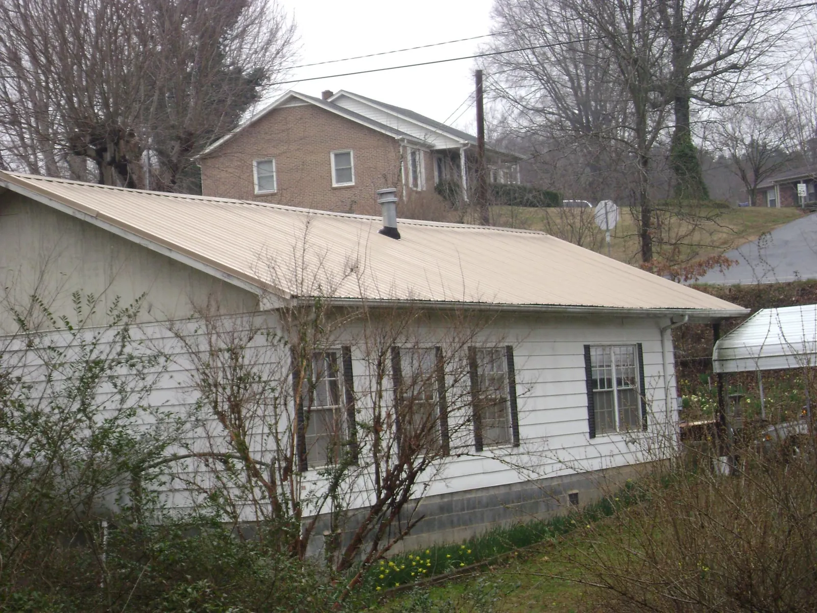 Tan metal roof on a white sided house set into a hillside — Commercial Roofing by Roofing Brothers in Peterman